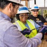 Two IBT trainees in hard hats and safety vests work together on a rooftop solar array