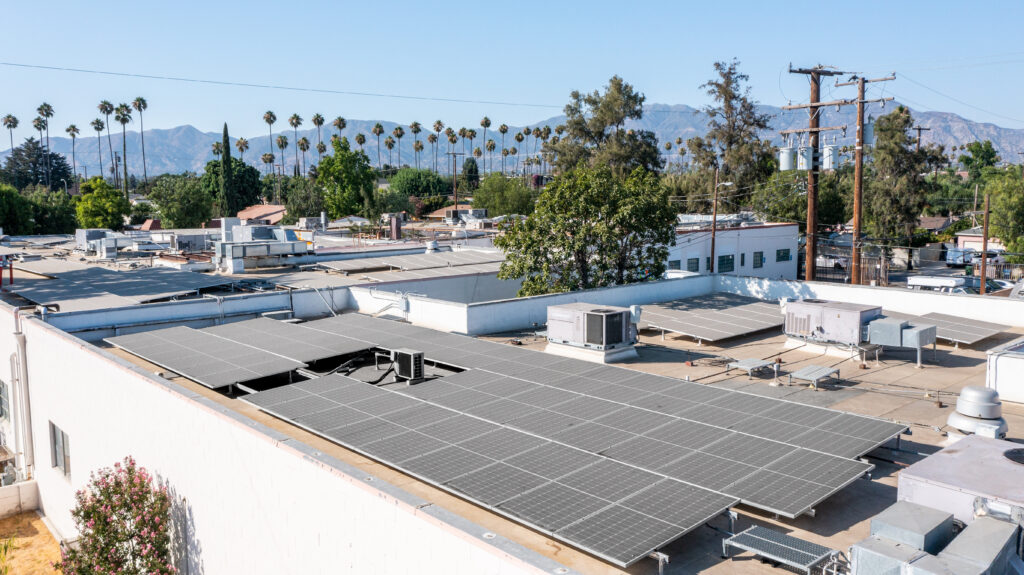 Rooftop solar panel array on white building with mountains and palm trees in background