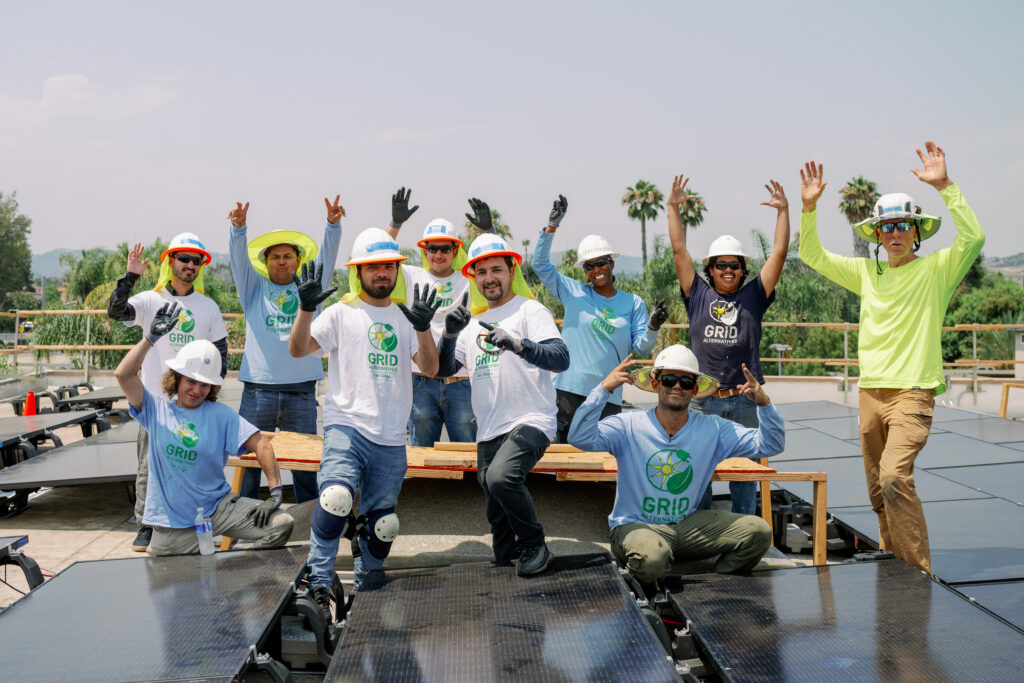 Team celebrates on solar panel installation, wearing GRID branded shirts and hard hats