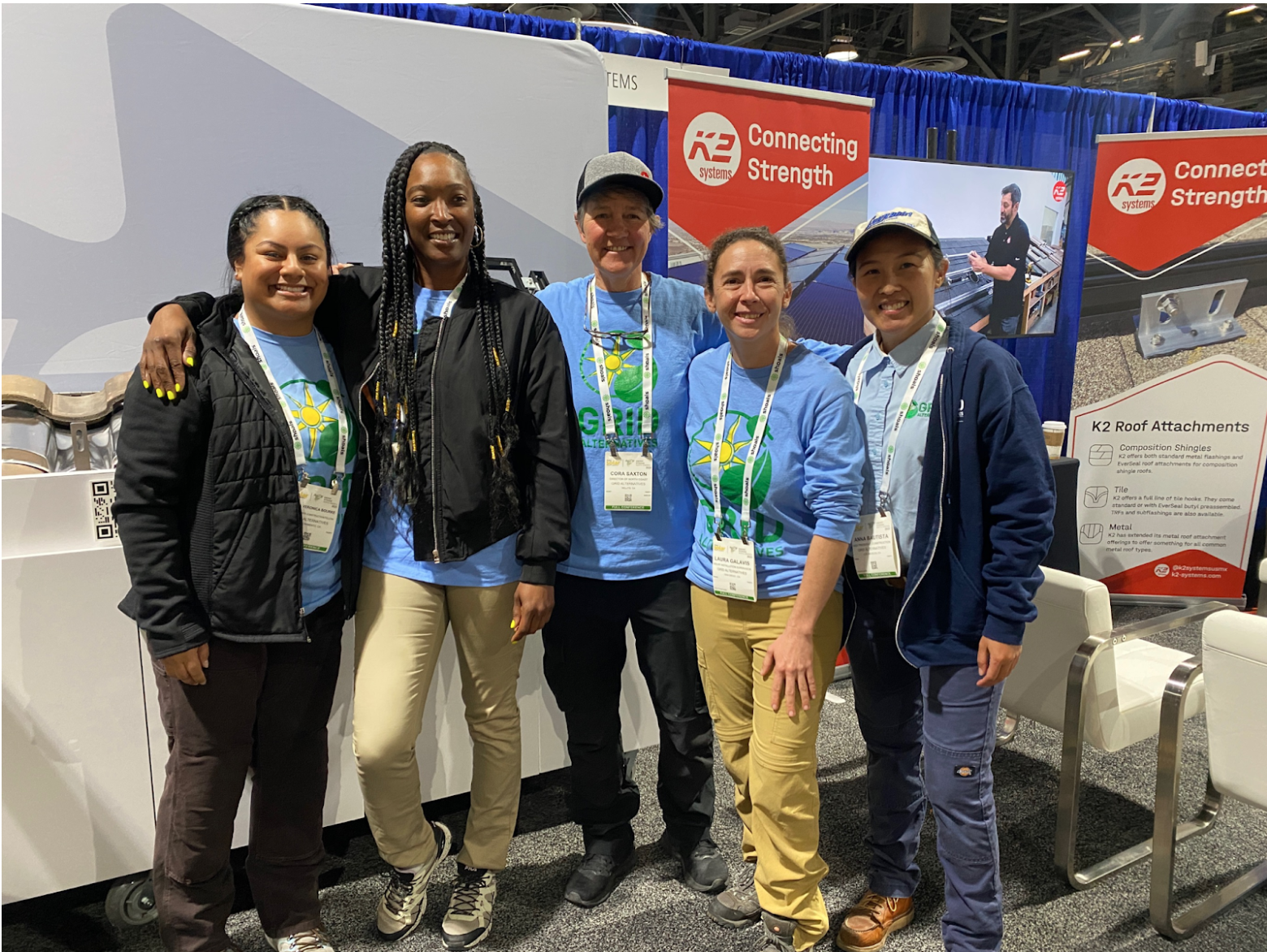 Five team members wearing lanyards pose together at a K2 "Connecting Strength" conference booth