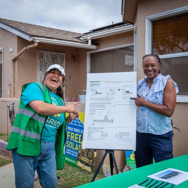 Two women smile while presenting a solar energy analysis document in front of a residential home