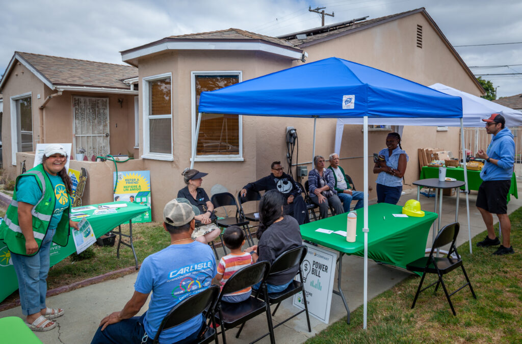 Community outreach event with blue tent, green tables, and volunteers engaging residents at a residential property